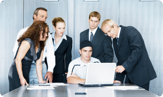A group of corporate employees surrounding a colleague with a laptop